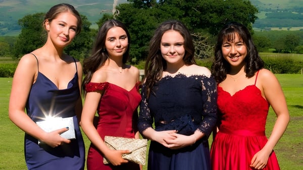 Cuatro jóvenes mujeres en ropa formal están frente a un paisaje montañoso en el terreno de St. Brigid's College.