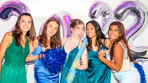 Cinco estudiantes en vestidos coloridos posan frente a grandes globos de 21 en color lila y plateado en el terreno de la St. Catherine's School.