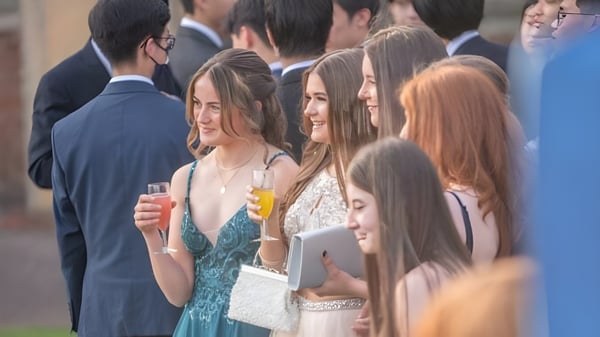Un grupo de personas bien vestidas se reúne en una fiesta en la St. Christopher School frente a un edificio de eventos.