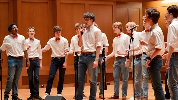 Un grupo de estudiantes de la St. Christopher’s School está junto y actúa en un escenario con revestimiento de madera.
