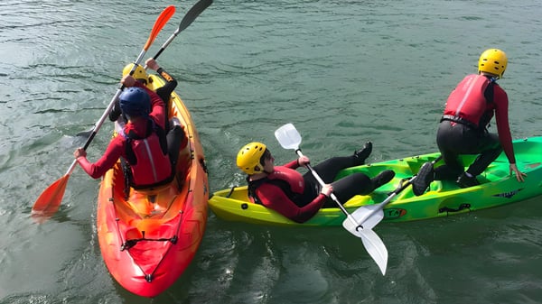 Estudiantes de la St. Ciarán’s Community School reman en coloridos kayaks en un lago en un entorno natural.