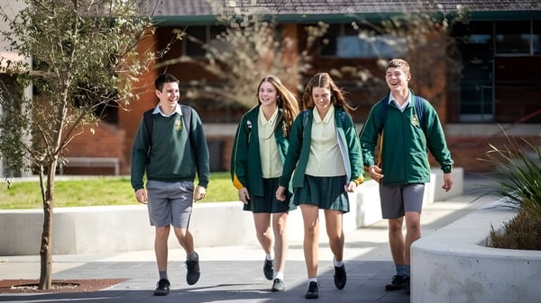 Cuatro alumnos de la St. Clare’s School caminan juntos por el campus escolar con un complejo de edificios al fondo.