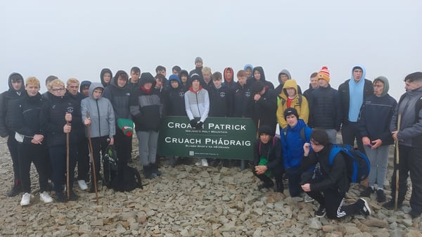 Un grupo de estudiantes del St. Coleman's College está frente al letrero de Croagh Patrick en un paisaje montañoso rocoso.