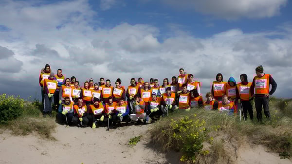 Un grupo de estudiantes está en un campo y lleva chalecos de seguridad naranjas en el terreno del St. Colman’s Community College.