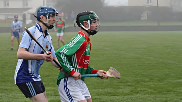 Dos alumnos en uniformes deportivos están en el campo deportivo del St. Colmans College frente a edificios.