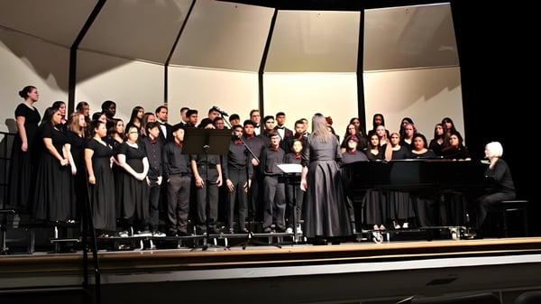Alumnos del St. Colmans College están juntos en un escenario con ropa formal y cantan junto a un piano en primer plano.