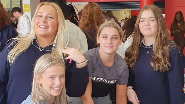 Un grupo de estudiantes sonrientes lleva sudaderas azules en el interior del campus de St. Conleths College.