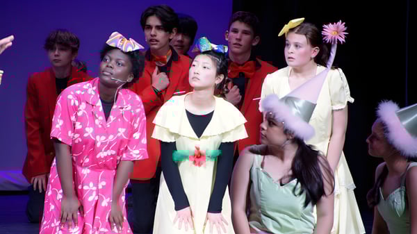 Estudiantes de la St. Croix Lutheran Academy están en coloridos disfraces en un escenario con fondo azul oscuro.