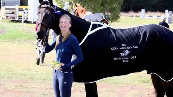 Una estudiante de St. Cuan’s College está en una pradera junto a un gran caballo negro.