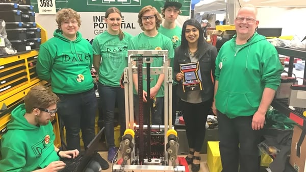 Un grupo de estudiantes de la St. David Catholic Secondary School está frente a una gran pancarta verde con la inscripción FIRST ROBOTICS COMPETITION.