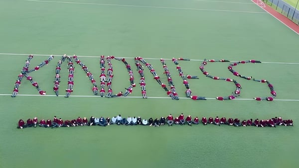 Un gran grupo de estudiantes de St. David's C.B.S. forma la palabra Kindness en el campo deportivo verde.
