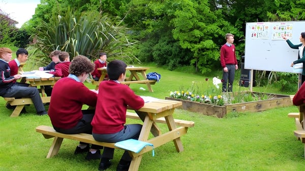 Estudiantes de St. David's C.B.S. están sentados en el área verde al aire libre durante una clase con pizarra blanca.