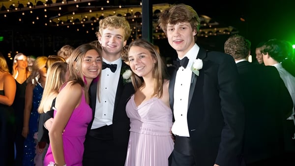 Un grupo de personas posan en un evento formal en el campus de St. David’s College frente a luces brillantes.