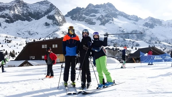 Un grupo de estudiantes de St. David's Catholic Sixth Form College posan frente a un paisaje montañoso nevado con una cabaña de esquí al fondo.