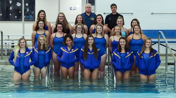 Un grupo de jóvenes nadadoras en trajes de baño azules en la piscina en el terreno de St. Dominic's Girl’s Catholic College con un entrenador al fondo.