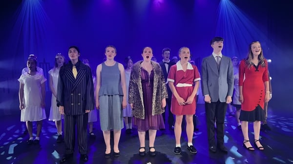 Un grupo de estudiantes de la St. Dominic's Grammar School presenta un desfile de moda en un escenario con iluminación azul-violeta.