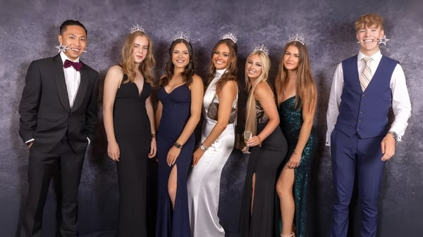 Un grupo de personas vestidas formalmente posan frente a un fondo oscuro en la foto de la St. Dominic's Grammar School.