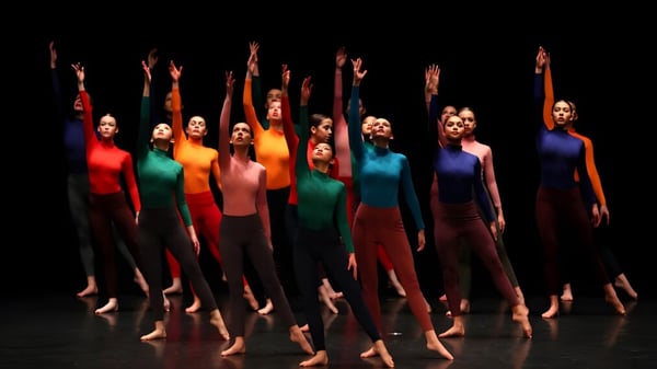 Estudiantes de la St. Edmunds School realizan un espectáculo de baile en trajes coloridos en un escenario oscuro.