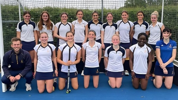 Un grupo de jóvenes atletas femeninas posan en el campo deportivo de la St Edward's School en Oxford frente a una cerca de alambre.