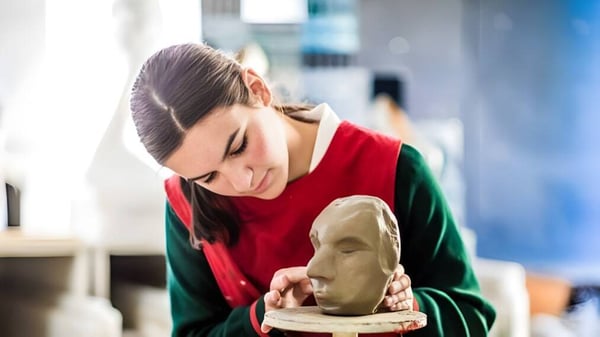 Un estudiante de St. Francis' College modela concentrado una figura de arcilla en un taller.