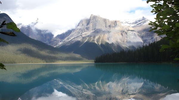 Un tranquilo lago de montaña con cumbres nevadas y vegetación verde se puede ver cerca de la St. Francis High School.
