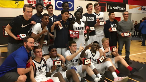 Un grupo de estudiantes de la St. Francis Xavier High School posan juntos en un gimnasio con logotipos de equipo de fondo.