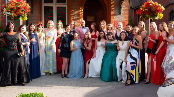 Un grupo de personas elegantemente vestidas está frente a un edificio de ladrillo en el campus de St. George's Ascot.