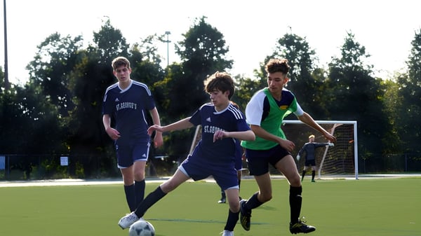Tres estudiantes juegan al fútbol en un campo de césped en el terreno de la St. George's School of Montreal.