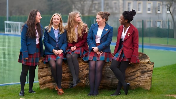 Un grupo de estudiantes de la St. George's School en uniforme escolar está junto en el campo deportivo frente a edificios.