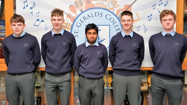 Cinco estudiantes en uniforme escolar están frente a un telón de fondo con el nombre St. Gerald's College y notas musicales.