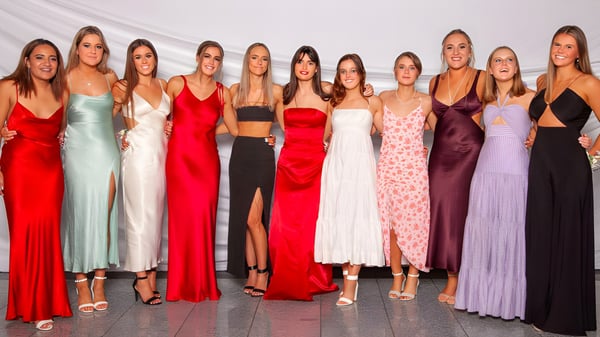 Un grupo de estudiantes en diferentes vestidos festivos posan frente a un fondo blanco en el campus de St. Hilda's Collegiate School.