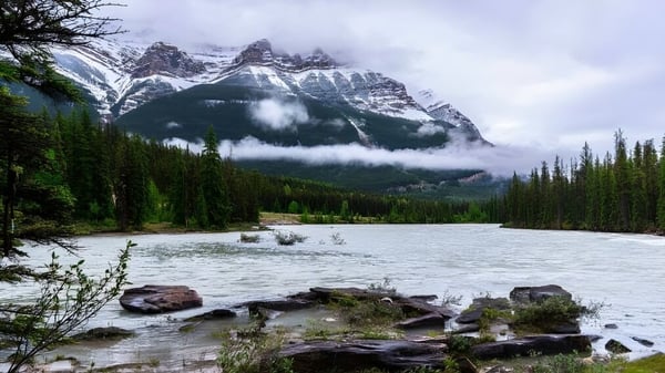 Un tranquilo lago de montaña con picos cubiertos de nieve y densos bosques en la orilla cerca del campus de St. James Collegiate.