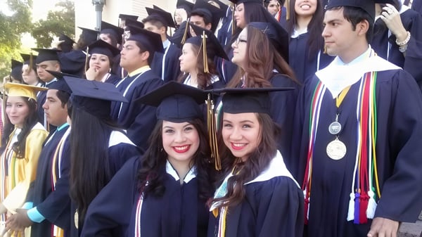 Un grupo de graduados de la St. John Paul II High School está al aire libre en vestimenta académica y sonríe a la cámara.