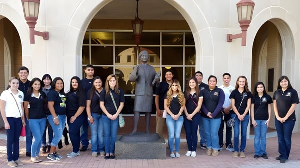 Un grupo de estudiantes posa frente al edificio de la St. John Paul II High School con arcos y iluminación decorativa.