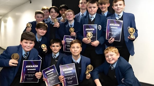 Un grupo de estudiantes del St. John Plessington Catholic College posan en el pasillo con varios premios y trofeos.