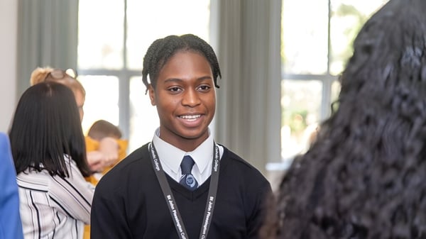 Un estudiante en uniforme escolar sonríe en el aula del St. John Plessington Catholic College con otros estudiantes al fondo.