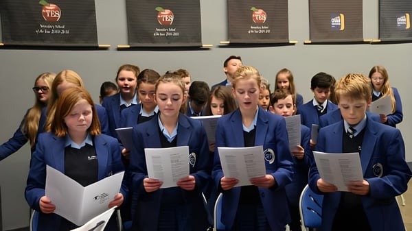 Estudiantes del St. John Plessington Catholic College están en uniforme escolar frente a estantes con libros y materiales.