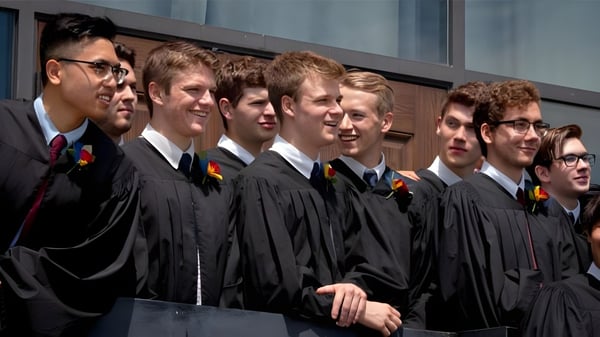 Un grupo de jóvenes en togas de graduación se encuentra frente a un edificio en el campus de la St. John’s-Kilmarnock School.