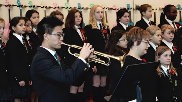 Un grupo de estudiantes de la St. John’s-Ravenscourt School está junto en uniformes escolares sosteniendo instrumentos musicales.