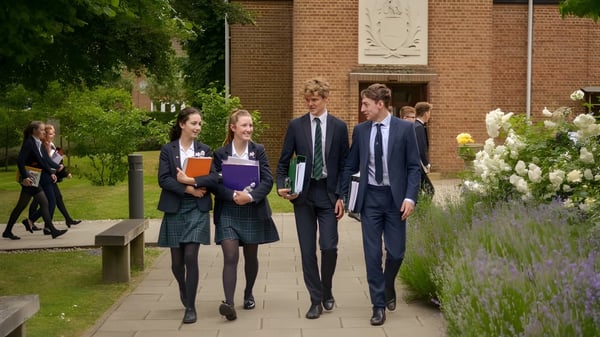 Un grupo de estudiantes camina juntos por un camino con entorno verde frente a un edificio de ladrillo en el campus de la St. John’s School en Leatherhead.