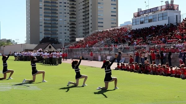 Estudiantes de la St. John's School se reúnen en uniformes rojos y blancos en el campo de deportes frente a edificios altos.