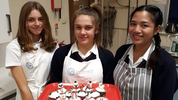 Tres estudiantes de la St. John’s School Sidmouth están juntas en una cocina escolar.