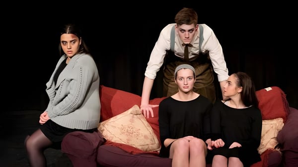 Un grupo de estudiantes de la St. John’s School está sentado en un sofá rojo frente a un fondo oscuro.