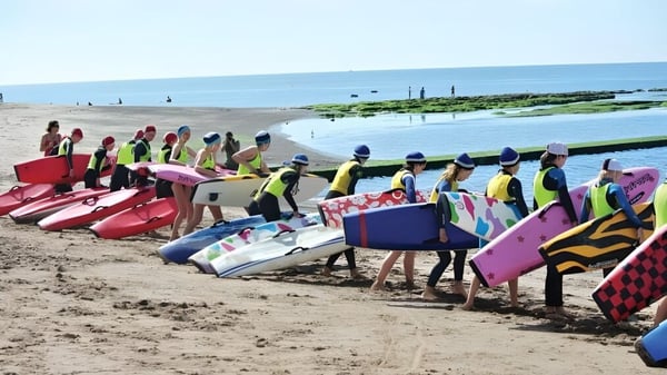 Un grupo de estudiantes de la St. John’s School en la playa lleva chalecos de salvamento coloridos y está frente al mar.