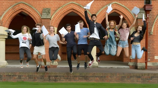 Un grupo de estudiantes de la St. John’s School en Leatherhead salta frente a un edificio de ladrillo con puertas en forma de arco.