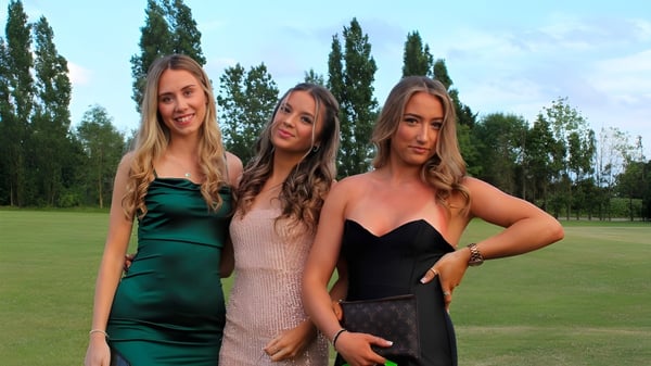 Tres alumnas del St. Joseph's College posan juntas en un prado con árboles de fondo.