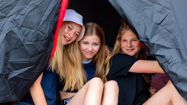 Tres alumnas con cabello largo y rubio están sentadas juntas en una construcción tipo tienda con un interior rojo en el campus del St. Joseph's College.