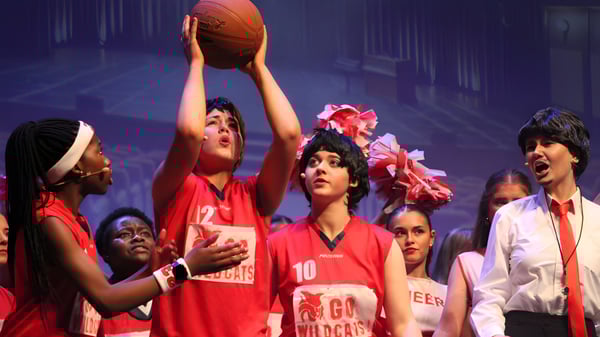 Un grupo de estudiantes de la St. Joseph’s Secondary School en Castlebar está de pie con camisetas rojas y un balón de baloncesto en un escenario frente a un fondo colorido.