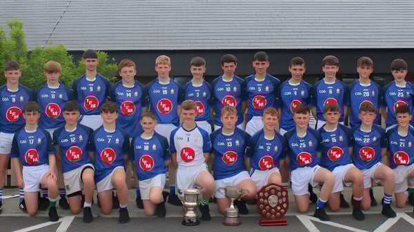 Un grupo de jóvenes atletas en camisetas azules posan con trofeos frente a un edificio en el terreno de la St. Joseph's Secondary School.