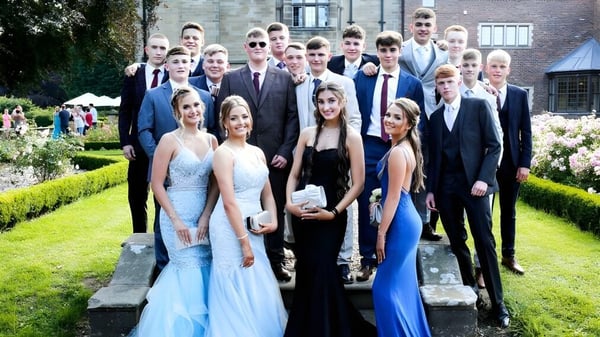 Un grupo de personas vestidas formalmente posan frente a un jardín verde en el campus del St. Lawrence College.